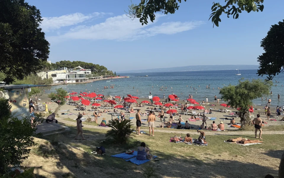 Sunbathers and red umbrellas on the sandy shallows of Bačvice beach in Split on a summer afternoon